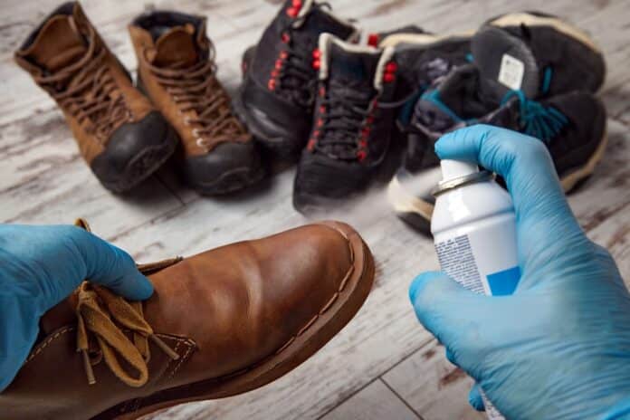 Hands in gloves spraying boots with other shoes in the background